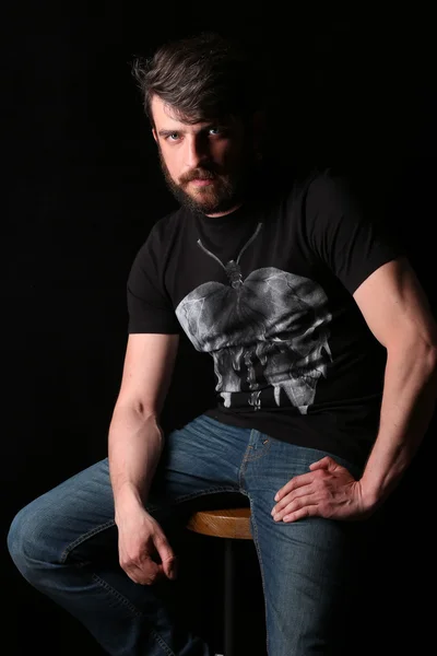 Bearded guy in T-shirt sitting on a bar stool. Close.up. Black