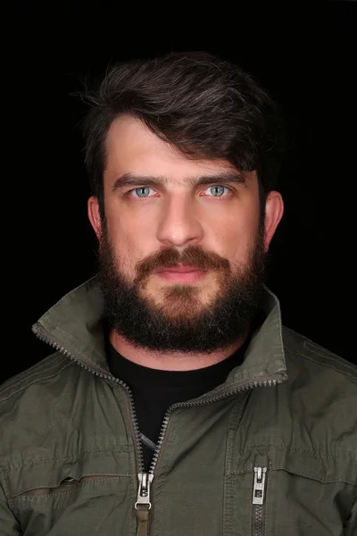 Bearded man in khaki jacket looking into the camera. Close.up. Black