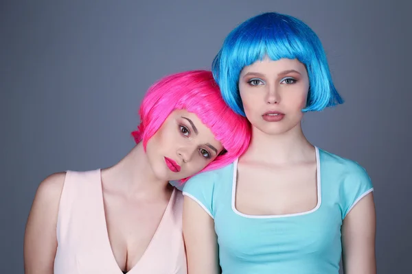 Teens in colorful wigs posing. Close up. Gray background