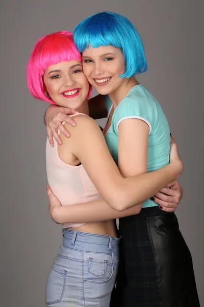 Smiling models in colorful wigs holding hands and posing. Close up. Gray background