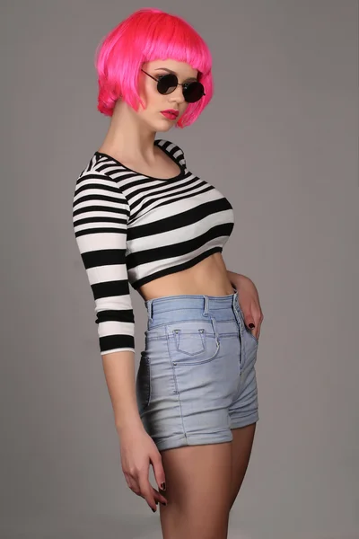 Model with circle sunglasses and pink wig. Close up. Gray background