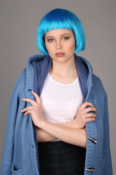 Girl in blue wig and coat posing with crossed arms. Close up. Gray background