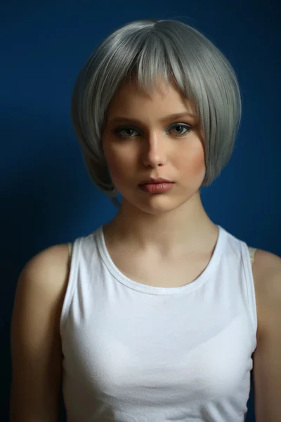 Girl in silver wig and white singlet posing . Close up. Blue background