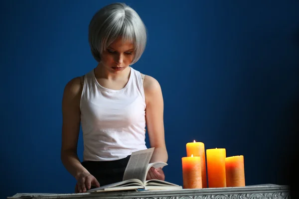 Teen model posing with book and candles. Close up. Blue background