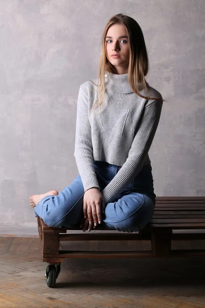 Girl in turtleneck sitting on a board. Gray background