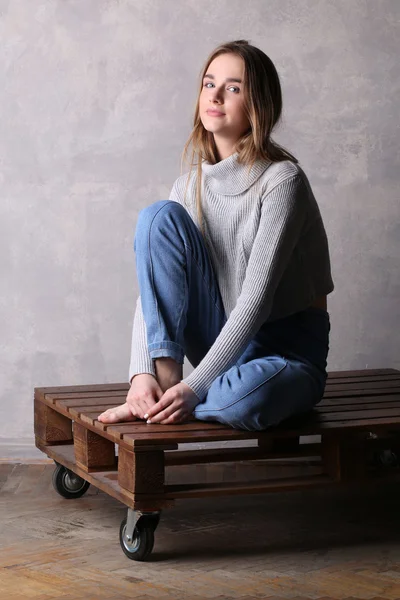 Girl with bended knee sitting on a deck. Gray background