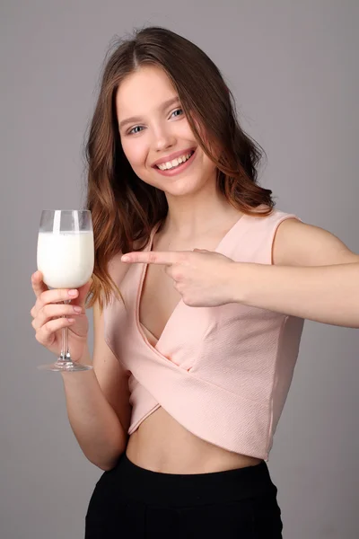 Girl points her finger at the bocal of milk. Close up. Gray background