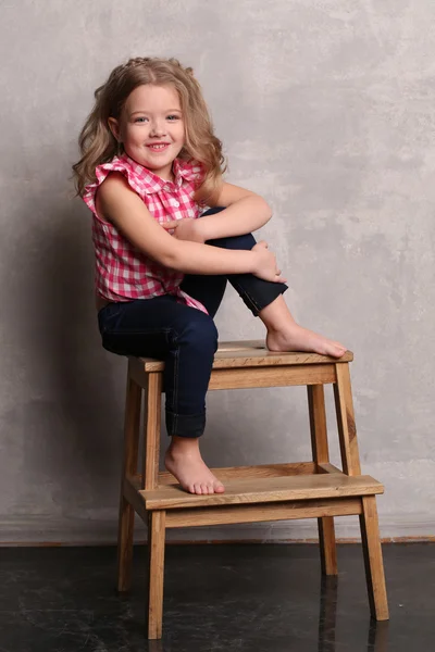 Portrait of a little girl with makeup posing on chair. Gray background
