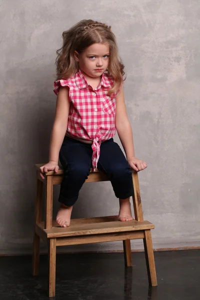 Portrait of a baby girl with makeup posing on chair. Gray background