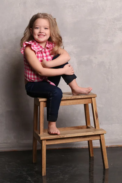 Portrait of a little lady with makeup posing on chair. Gray background