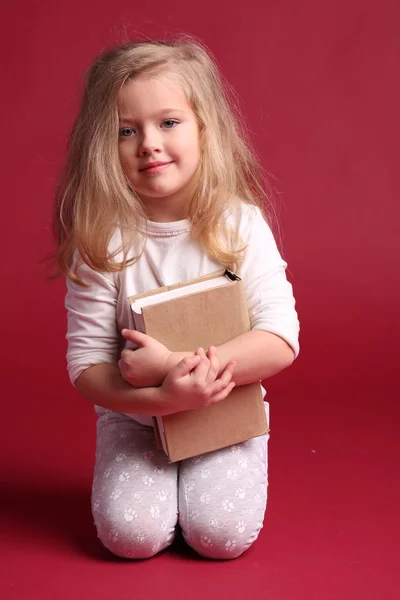 Sitting blonde in pajamas hugging a book. Red background