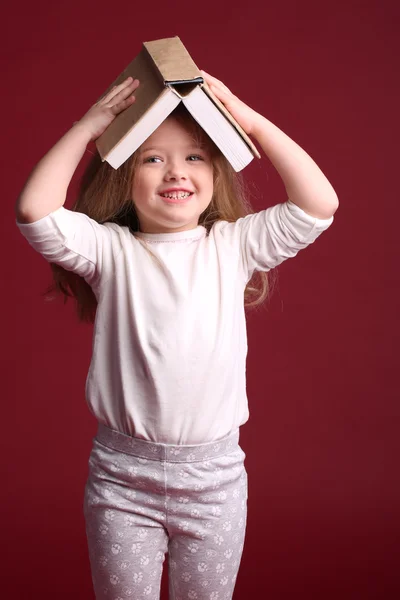 Girl in pajamas with a book on her head. Close up. Red background