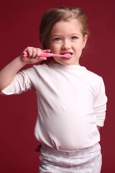 Baby brushing her teeth. Close up. Red background
