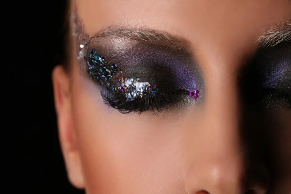 Womans smokey eye with colorful crystals. Close up. Black background