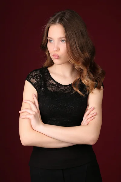 Girl in black dress with crossed arms. Close up. Dark red background