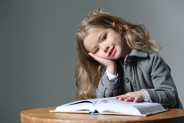 Little lady sitting at the table with a book. Close up. Gray background