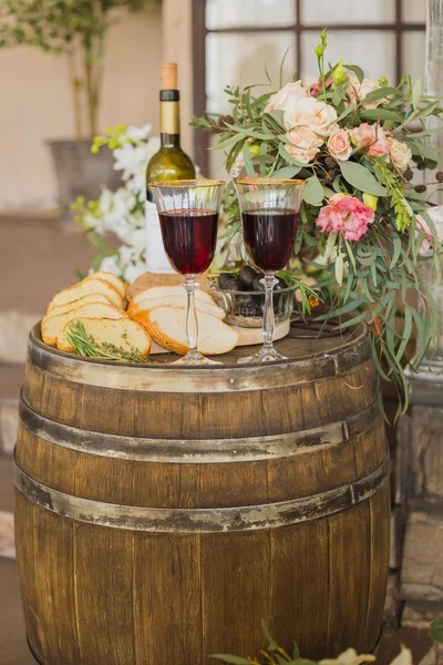 Black olives in glass vase, bread and vine, flowers on old oak barrel