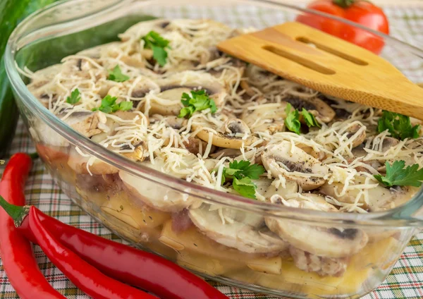 Baked potato slices with mushrooms in a transparent bowl for baking.