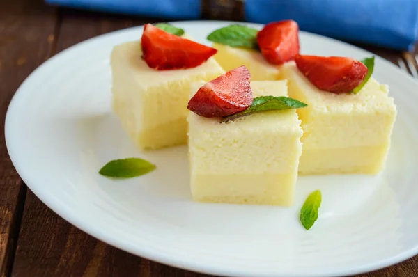 Delicate cottage cheese and creamy souffle in the form of cubes, decorating with mint leaves and fresh strawberries on a white plate