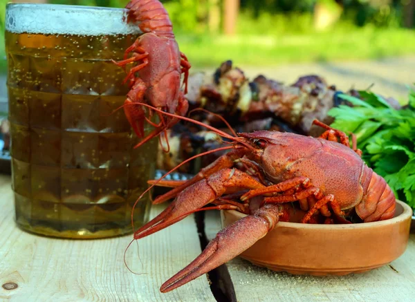 Foamy beer in a glass and boiled crawfish closeup, grilled meat on skewers in the background. For the holidays, enjoying the outdoors