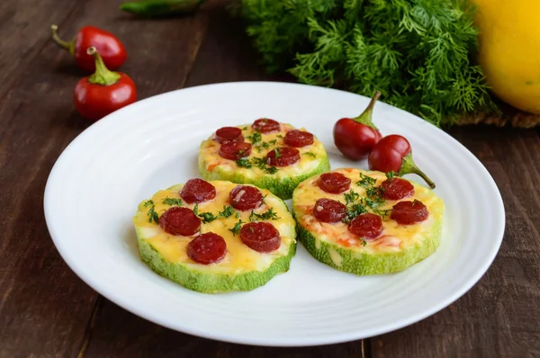 Small zucchini pizza on the circles with pepperoni and mozzarella. On a dark wooden background.