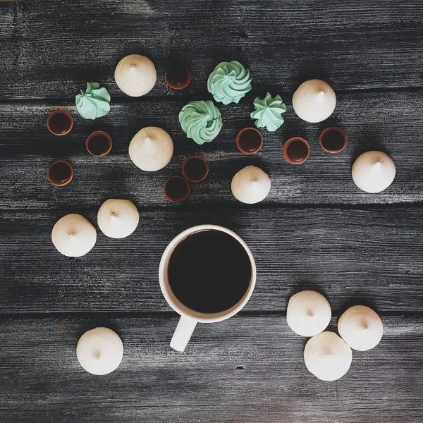 Cup of black coffee with white and mint cakes and black background