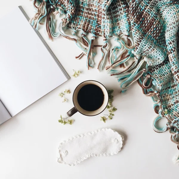 Cup of black coffee, white sleep mask, mint plaid, magazine and green leaves isolated on white background. Overhead view