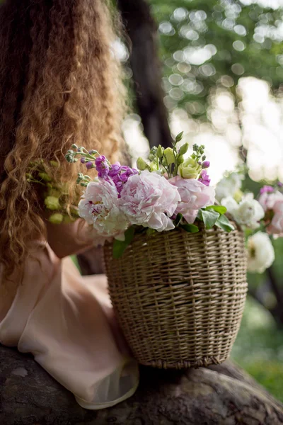 Curly girl sitting on a tree with basket of flowers