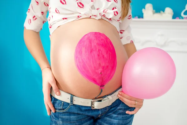 Belly of a pregnant woman , pink ball painted on the belly and pink ball in hand