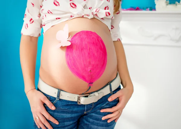 Belly of a pregnant woman , pink ball painted on the belly and pink butterfly attached to the ball