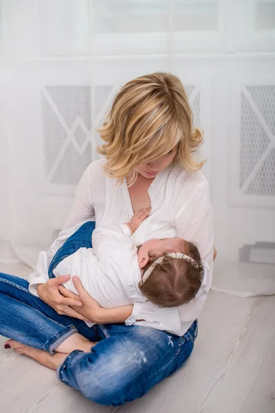 Happy mom breastfeeding her child baby girl lying on her breast and feeding on a whine background