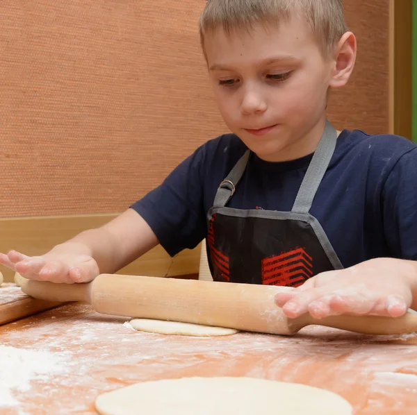 Young boy  rolling dough with a large wooden rolling pin as he prepares the cakes