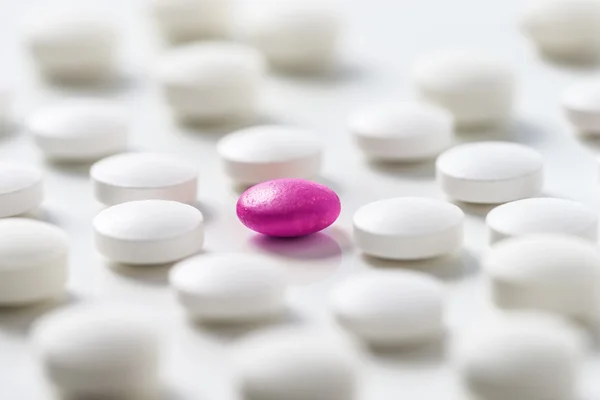 White pills  with a pink one  on white backgroung background.