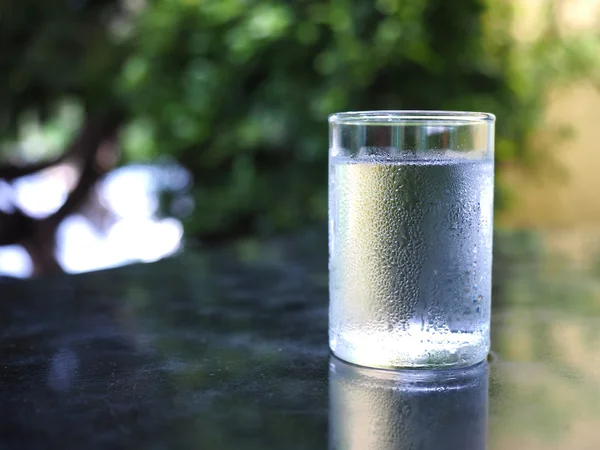 A glass of cool drinking water with green nature background