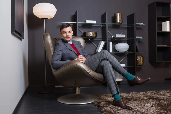 Fashionable young man sitting on a chair putting one leg on another