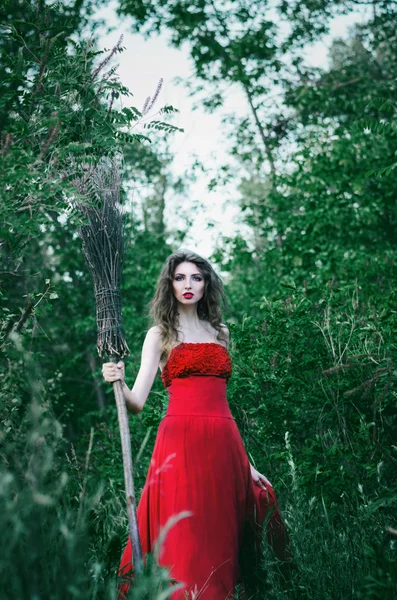 Beautiful girl witch in red dress in one hand holding a broom and goes ahead