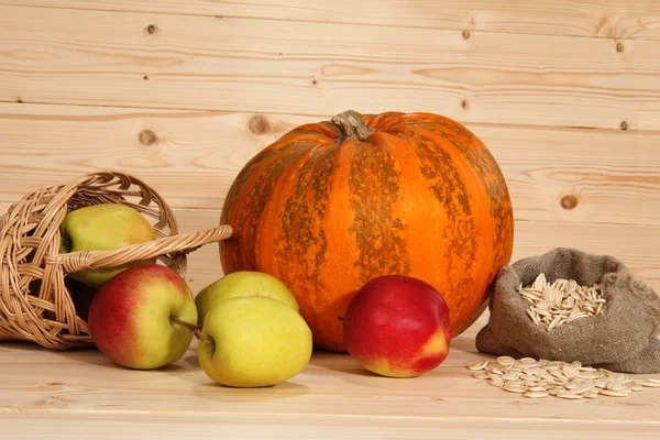 Pumpkin, pottle with apples and bag with seeds on wooden backgro