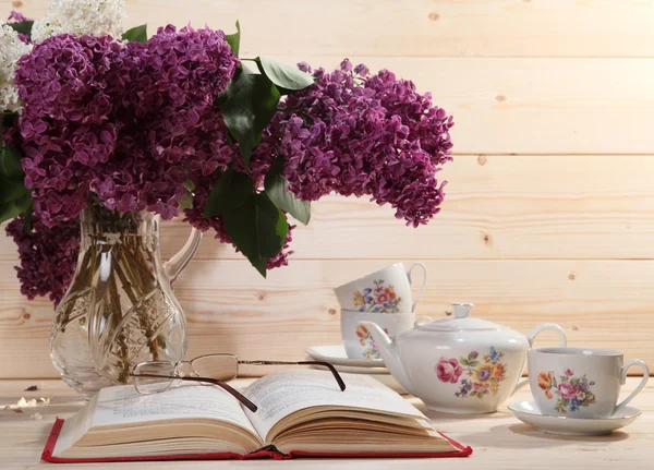 Bouquet of lilacs, open book, spectacles, teapot and cup of tea