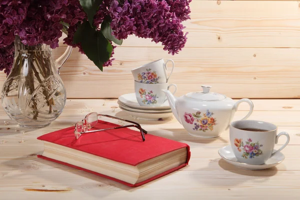 Bouquet of lilacs, book, spectacles, teapot and cup of tea