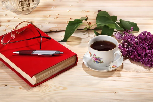 Cup of tea, branch of lilacs, book, spectacles and pen