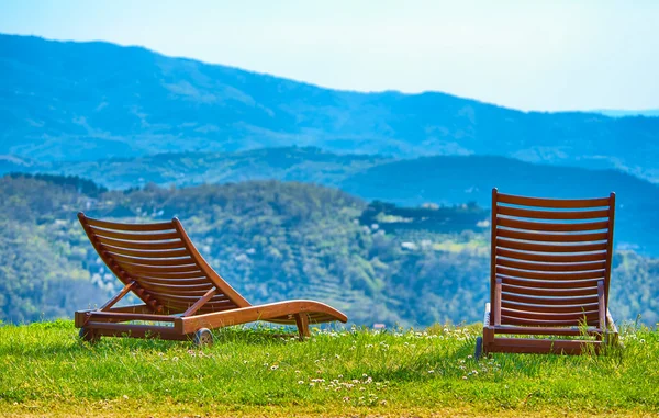 The two reclining chairs sit on the grass overlooking the valley and the hills