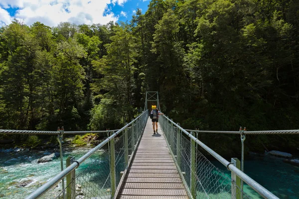 Woman hiker with backpack walking on suspension bridge