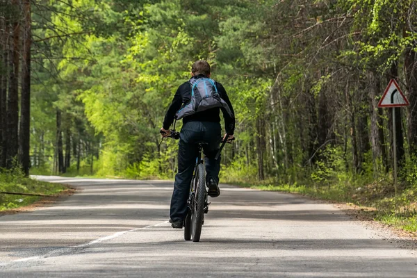 Cyclist rides along the road in the forest