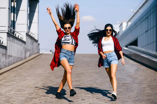 Two young happy hipster girls in sunglasses having fun, smiling, laughing, jumping, walking outdoor on the street, summer relax concept