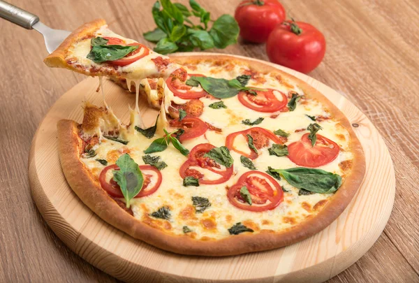 Pizza Margherita with tomatoes, mozzarella and basil on a wooden background, a slice of pizza with cheese stretching