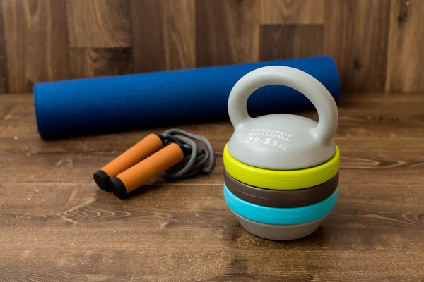 Adjustable kettlebell, jumping rope and mat for fitnes on wooden background. Weights for a fitness training.