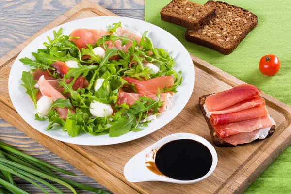 Arugula, prosciutto, mozzarella salad on a white dish