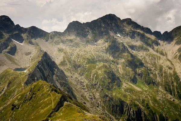 Mountainside with rocky slopes, peaks with cloudy sky in a background and trail from the lake in Carpathian Mountains in Romania