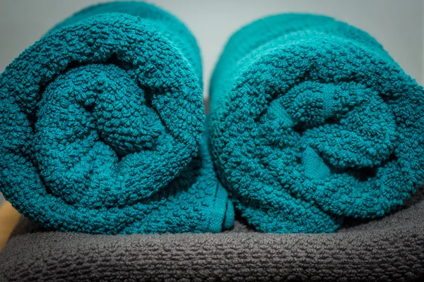 Rolled up turquoise towels located on a gray towel