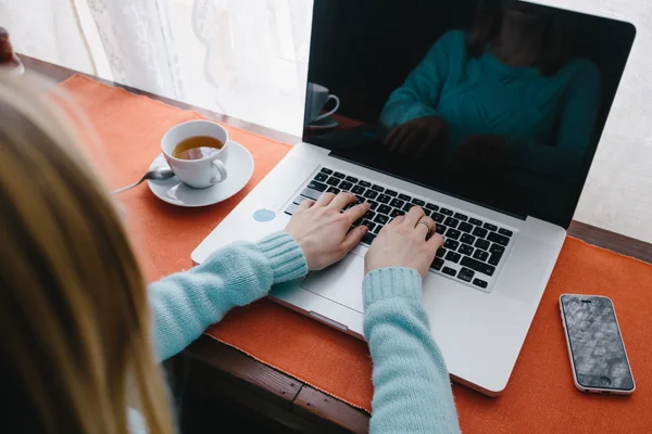 Woman typing on keyboard of a laptop with a coffee cup on table.